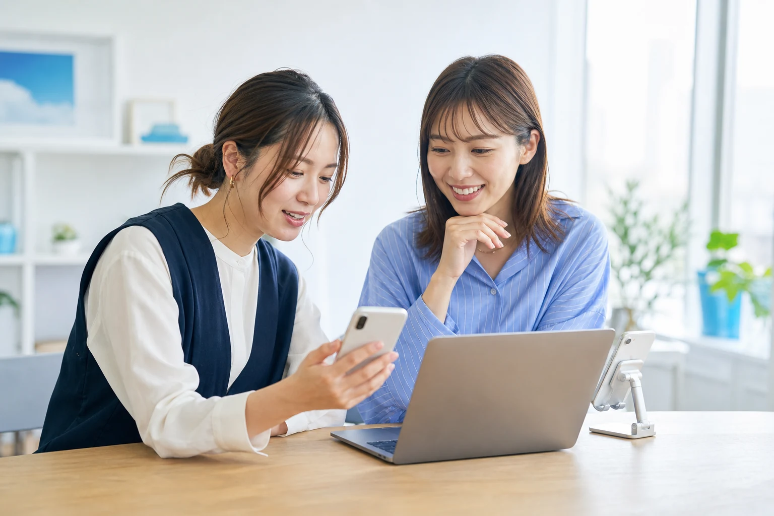 スマートフォンとノートパソコンを使いSNS企画を相談する2人の女性
